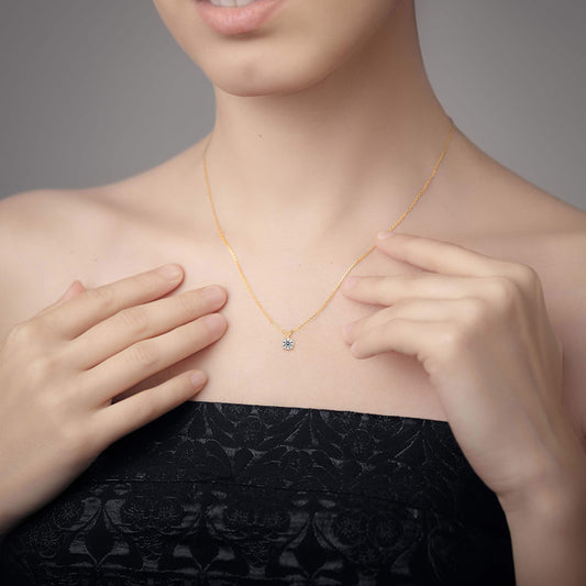 Person wearing a gold solitaire diamond pendant necklace, hands adjusting it.