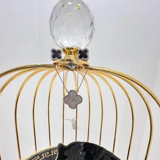 A gold diamond pendant with earrings set, featuring a chain of inset diamonds on a gold-colored metal structure, displayed on a glass stand.