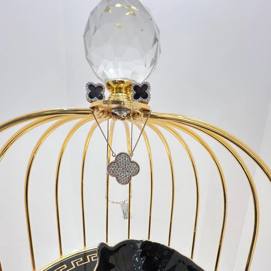 A gold diamond pendant with earrings set, featuring a chain of inset diamonds on a gold-colored metal structure, displayed on a glass stand.