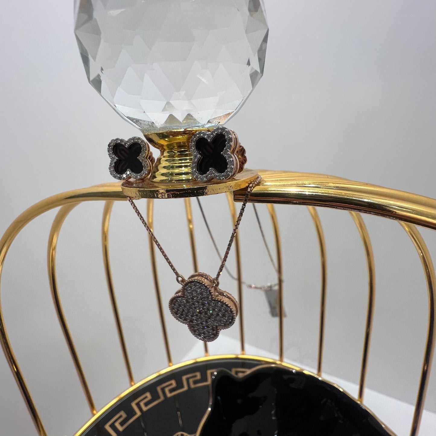 A gold diamond pendant with earrings set, featuring a chain of inset diamonds on a gold-colored metal structure, displayed on a glass stand.