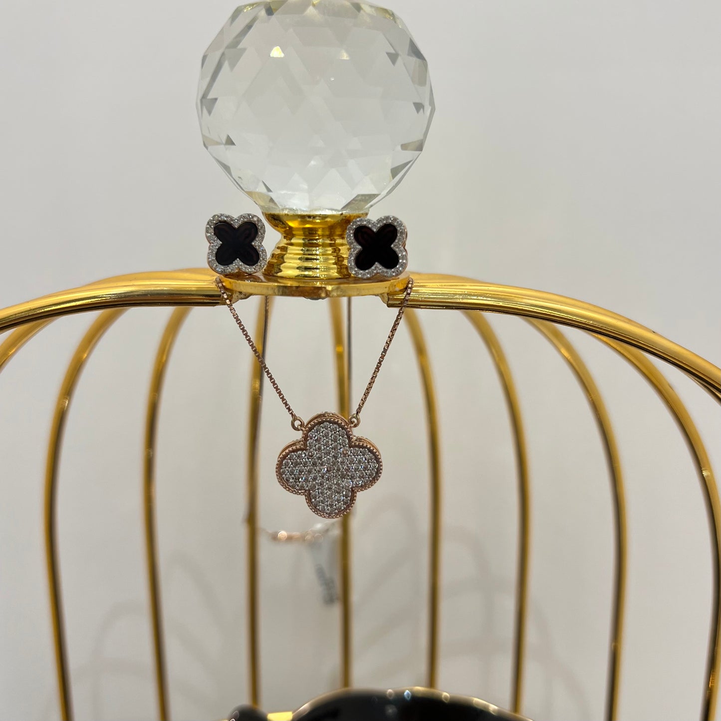 A gold diamond pendant with earrings set, featuring a chain of inset diamonds on a gold-colored metal structure, displayed on a glass stand.