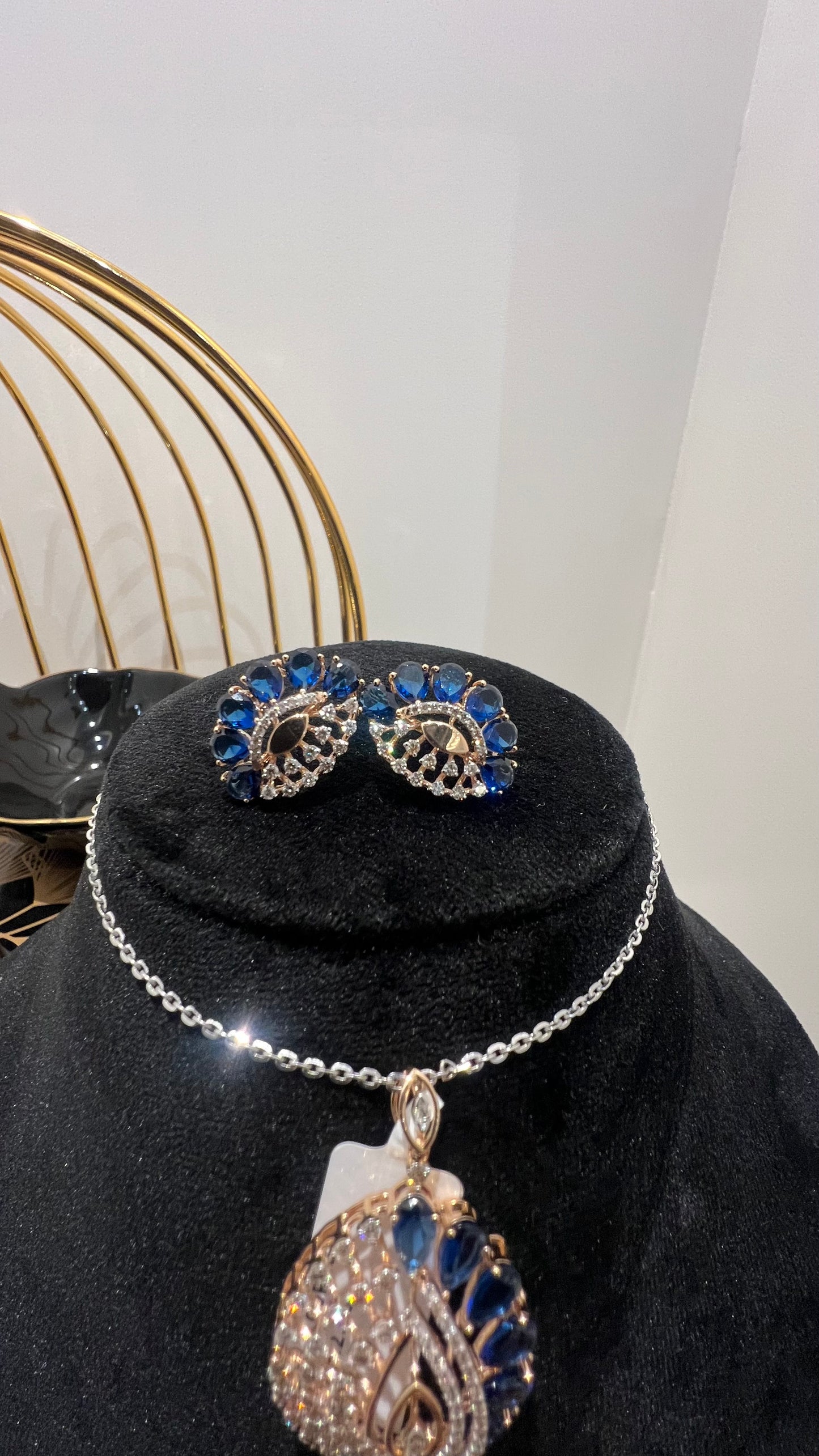 A gold diamond pendant with blue stone accompanied by matching earrings, displayed on a black mannequin bust.