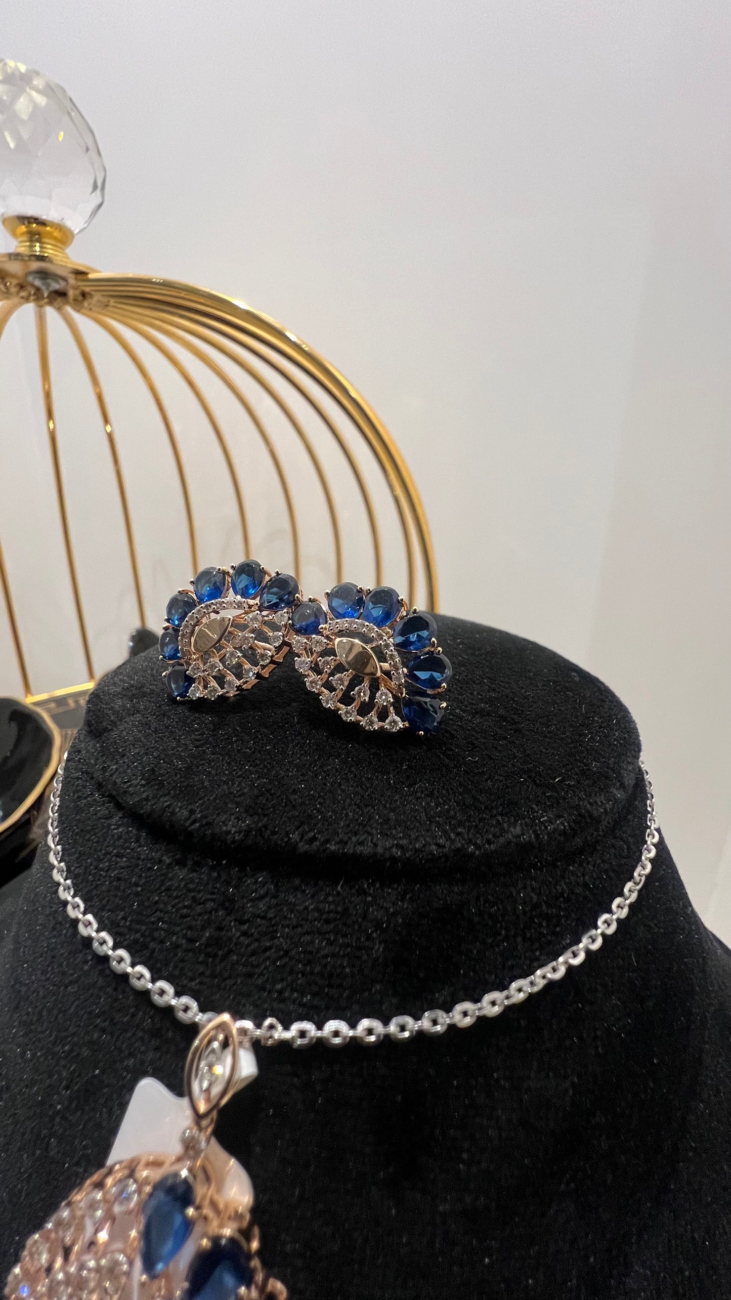 A gold diamond pendant with blue stone accompanied by matching earrings, displayed on a black mannequin bust.