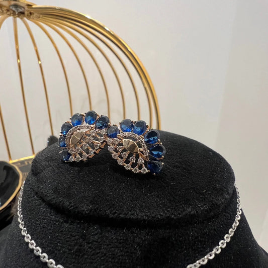 A gold diamond pendant with blue stone accompanied by matching earrings, displayed on a black mannequin bust.