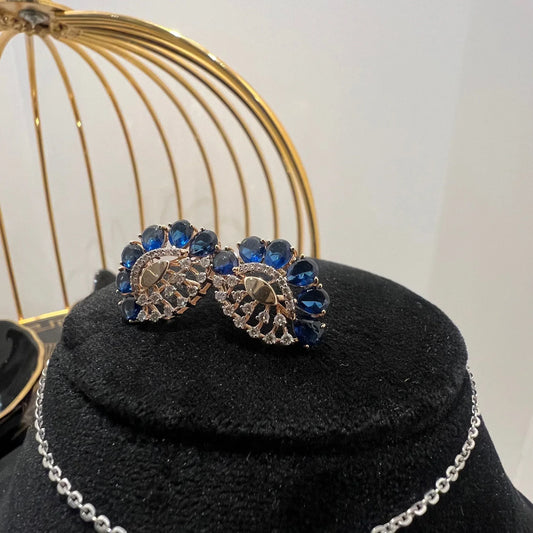 A gold diamond pendant with blue stone accompanied by matching earrings, displayed on a black mannequin bust.