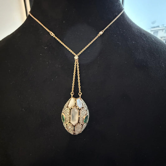 Oval-shaped gold diamond pendant with emerald green accents and mosaic design on a fine gold chain.