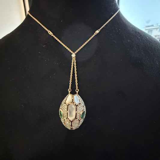 Oval-shaped gold diamond pendant with emerald green accents and mosaic design on a fine gold chain.
