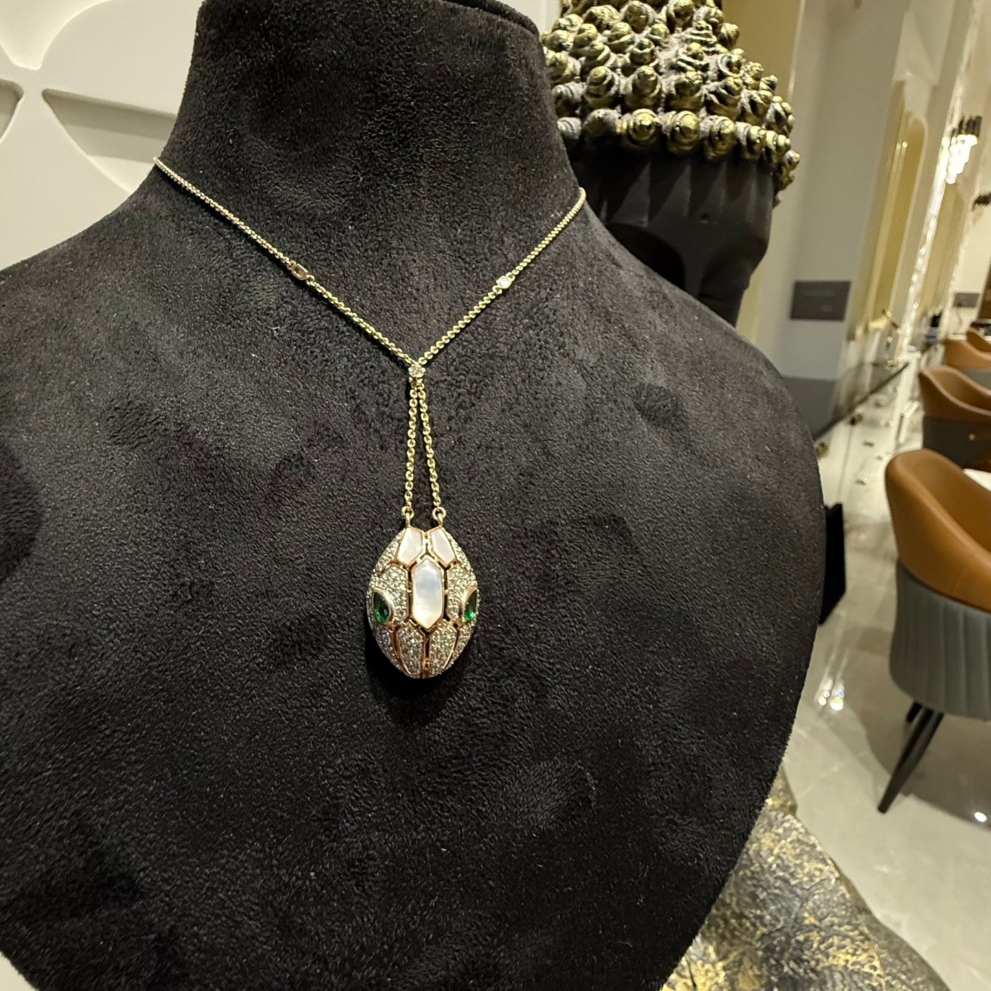 Oval-shaped gold diamond pendant with emerald green accents and mosaic design on a fine gold chain.