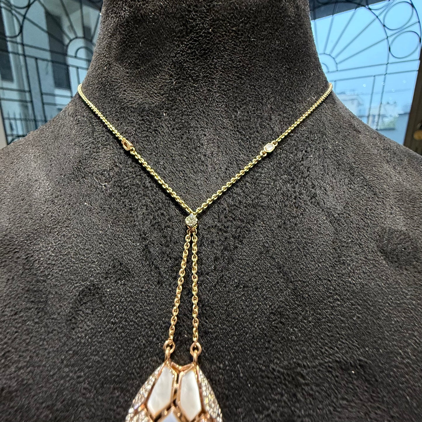 Oval-shaped gold diamond pendant with emerald green accents and mosaic design on a fine gold chain.