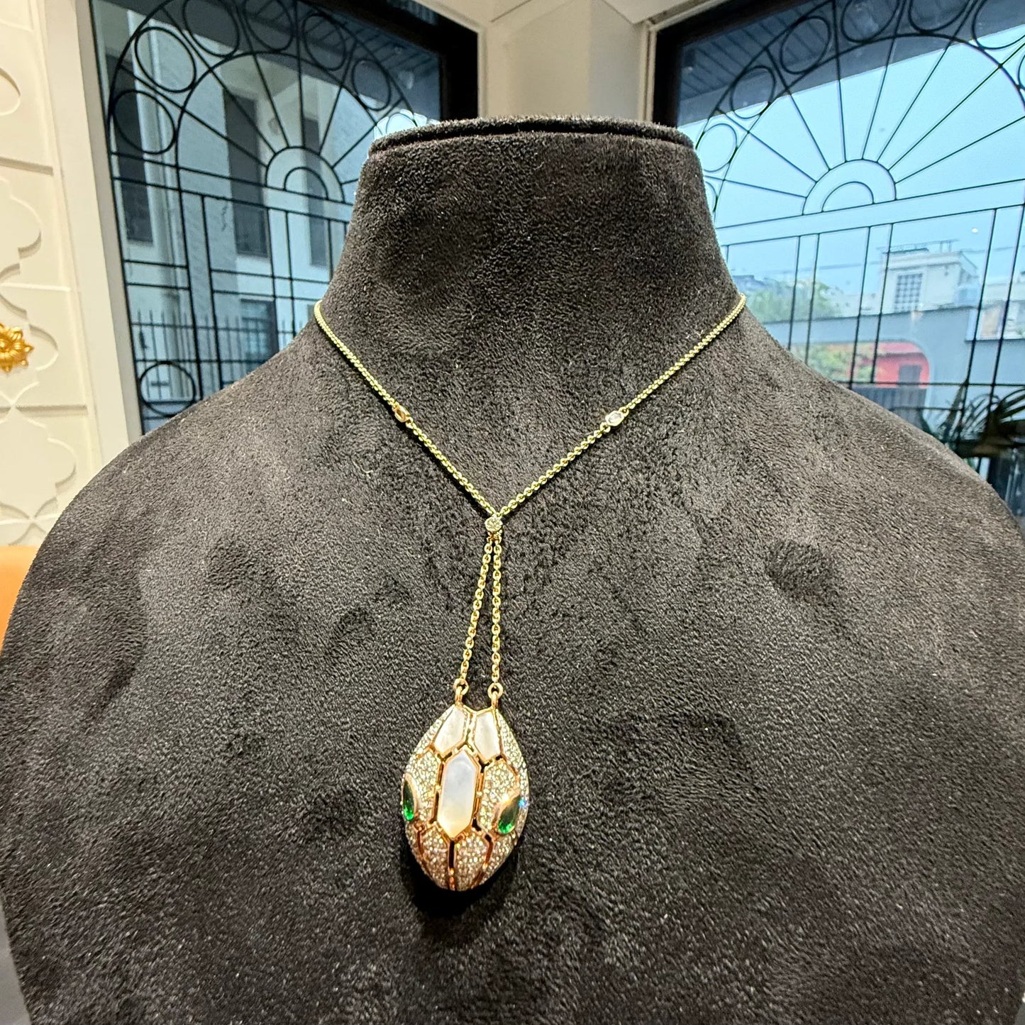 Oval-shaped gold diamond pendant with emerald green accents and mosaic design on a fine gold chain.