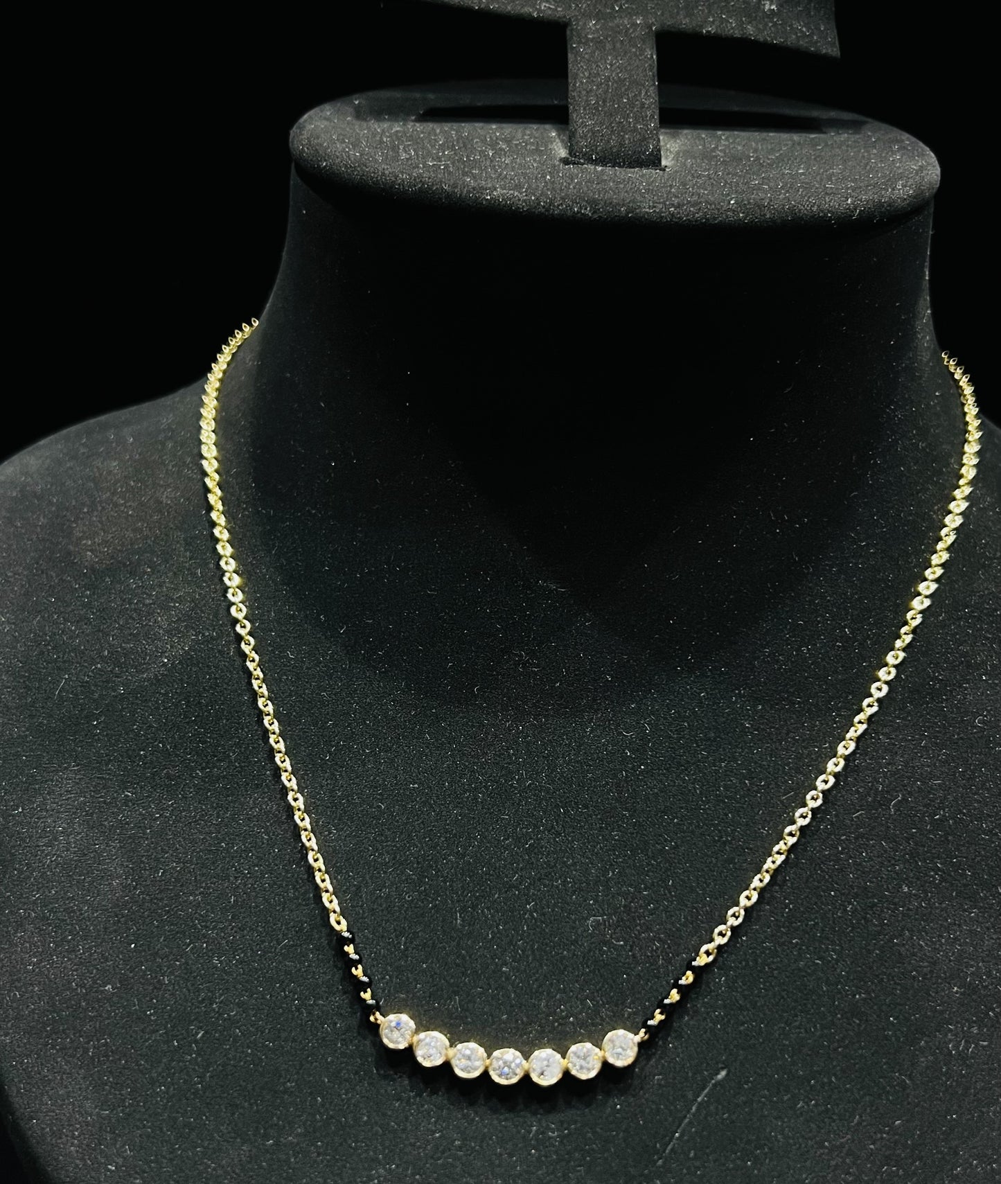 A stylish gold diamond beaded mangalsutra with seven round bezel-set diamonds in a row, paired with small black beads on a delicate gold chain.