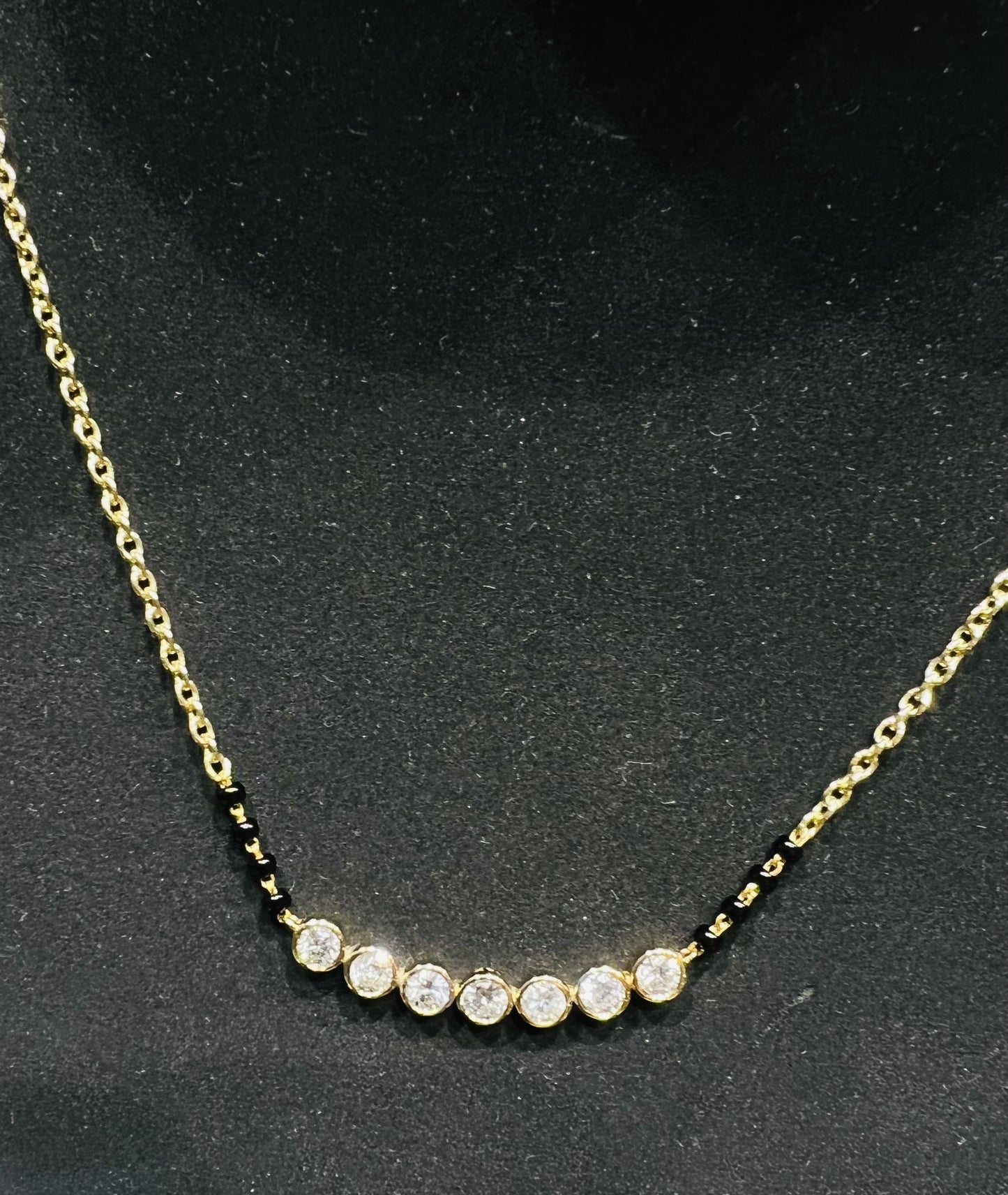 A stylish gold diamond beaded mangalsutra with seven round bezel-set diamonds in a row, paired with small black beads on a delicate gold chain.