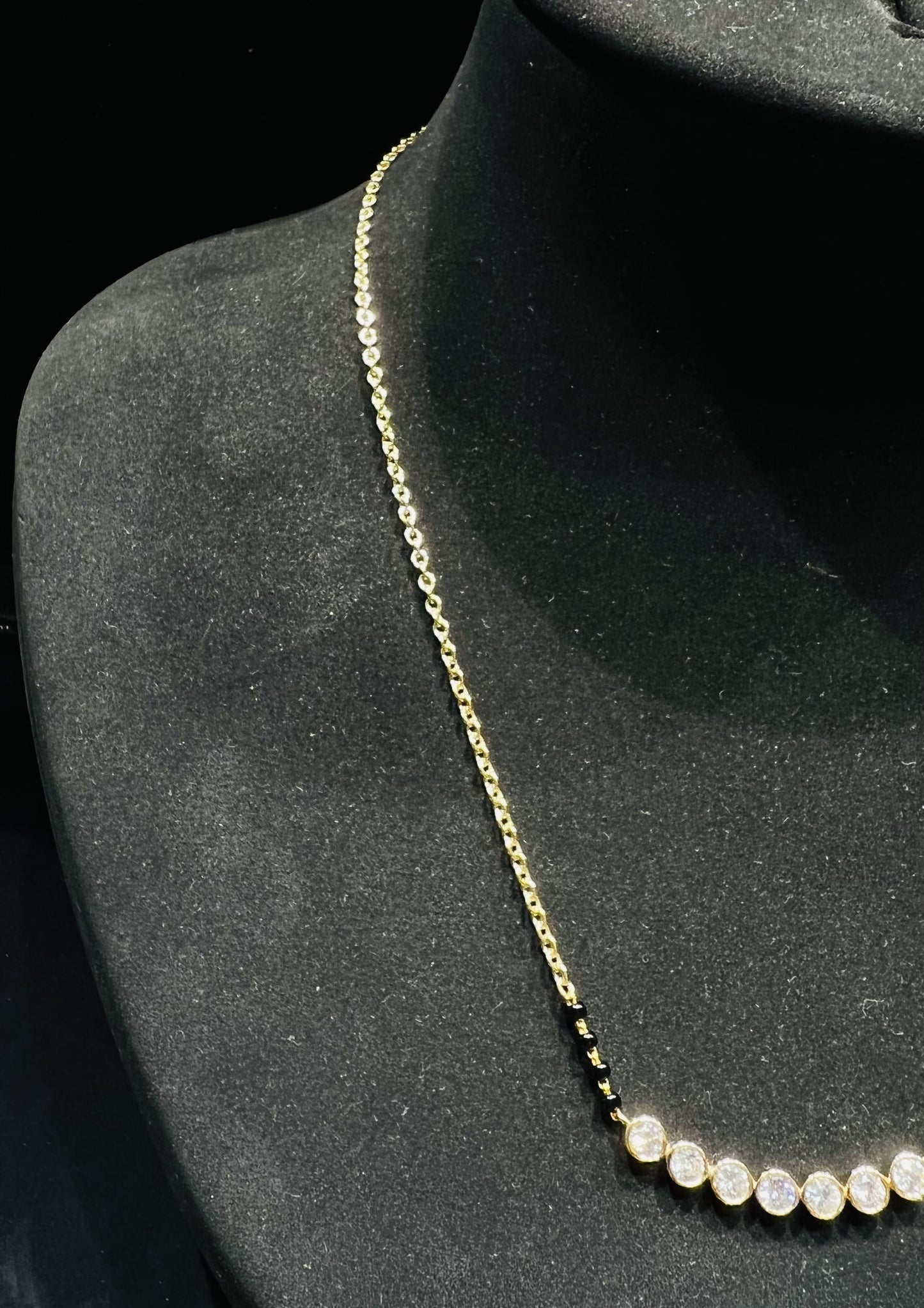 A stylish gold diamond beaded mangalsutra with seven round bezel-set diamonds in a row, paired with small black beads on a delicate gold chain.