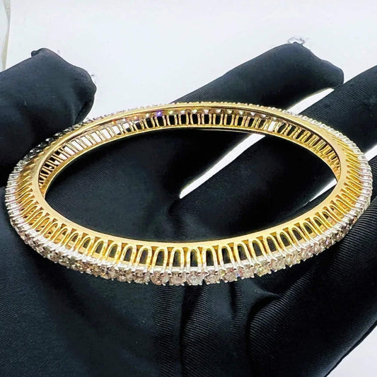 Gold bangles with lab grown diamond accents on a black gloves worn hand against a white background.
