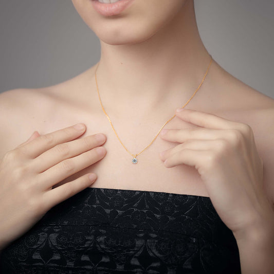 Person wearing a gold solitaire lab grown diamond pendant necklace, hands adjusting it.