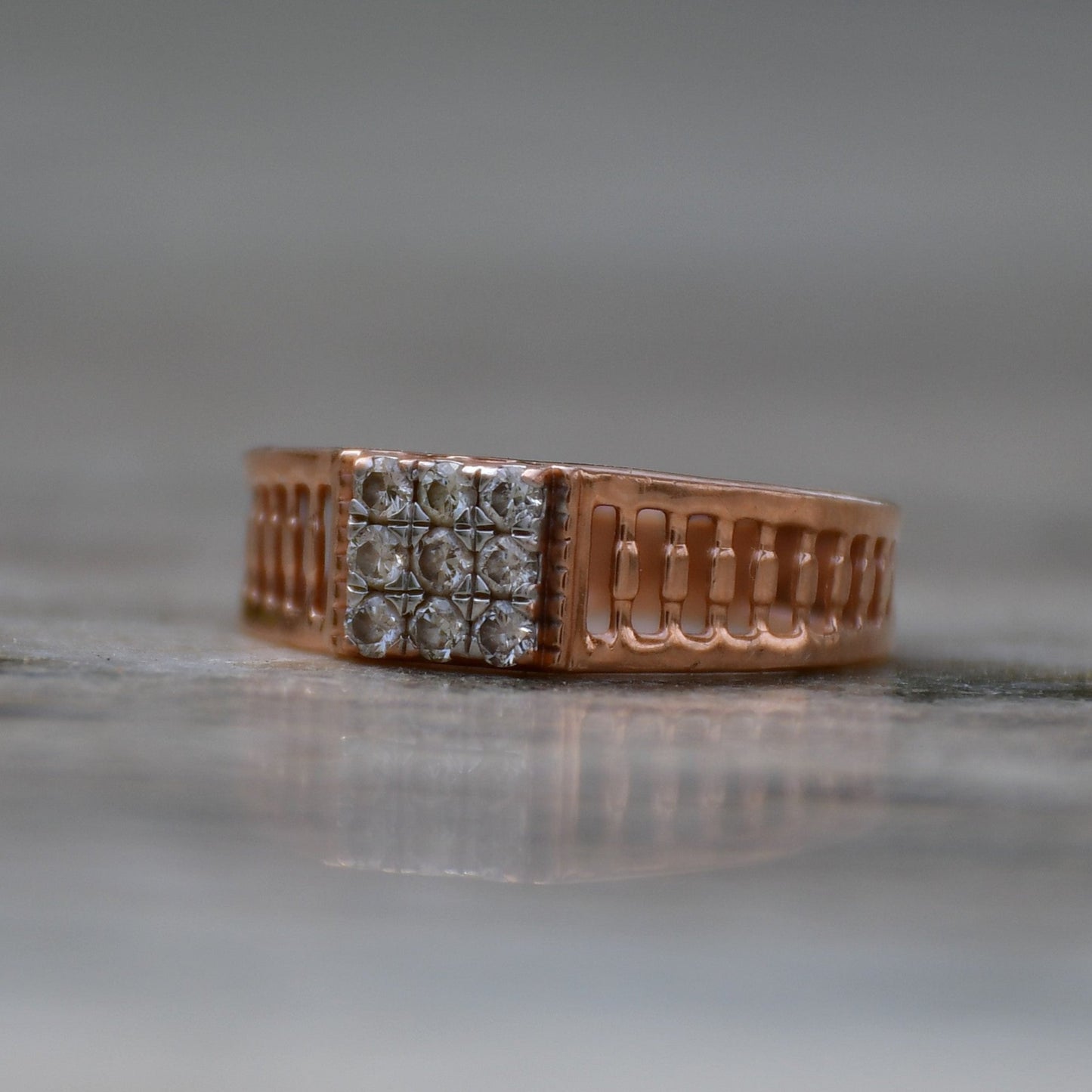 A gold diamond ring is displayed on a grey surface.