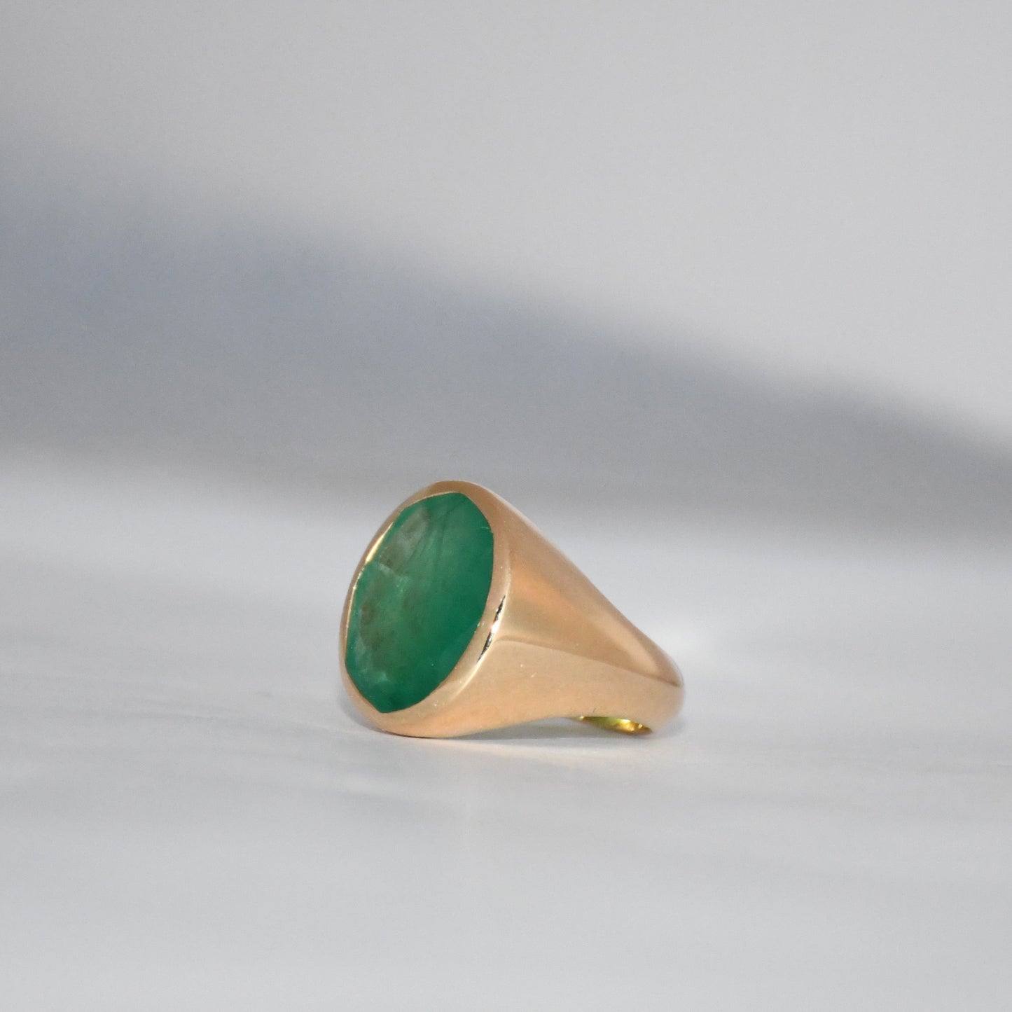 Gold ring with a green emerald stone on a gray background