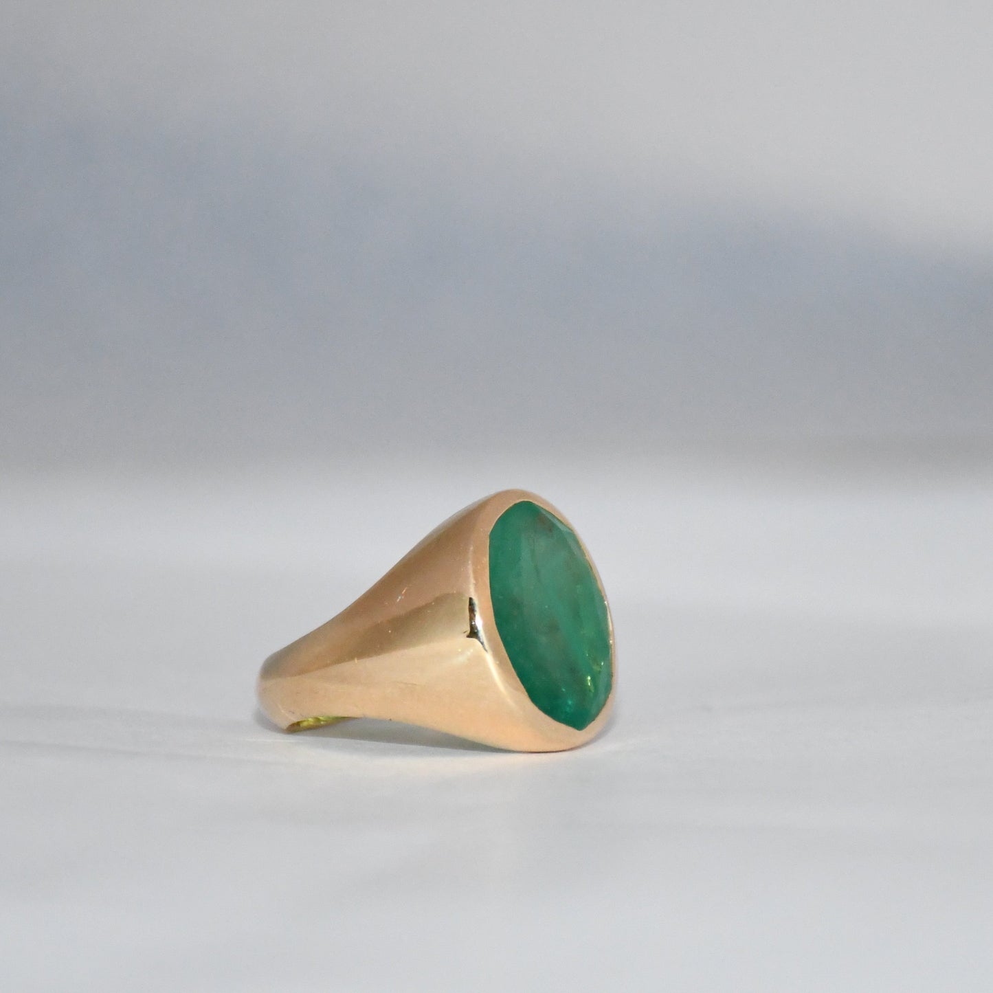 Gold ring with a green emerald stone on a gray background