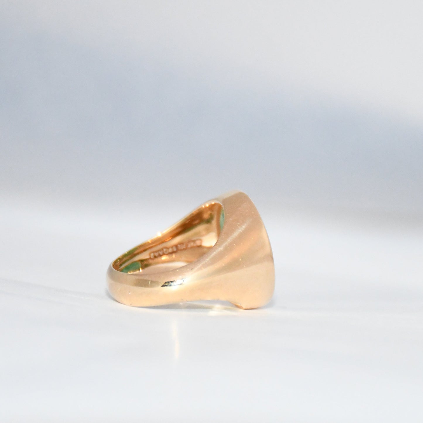 Gold ring with a green emerald stone on a gray background.