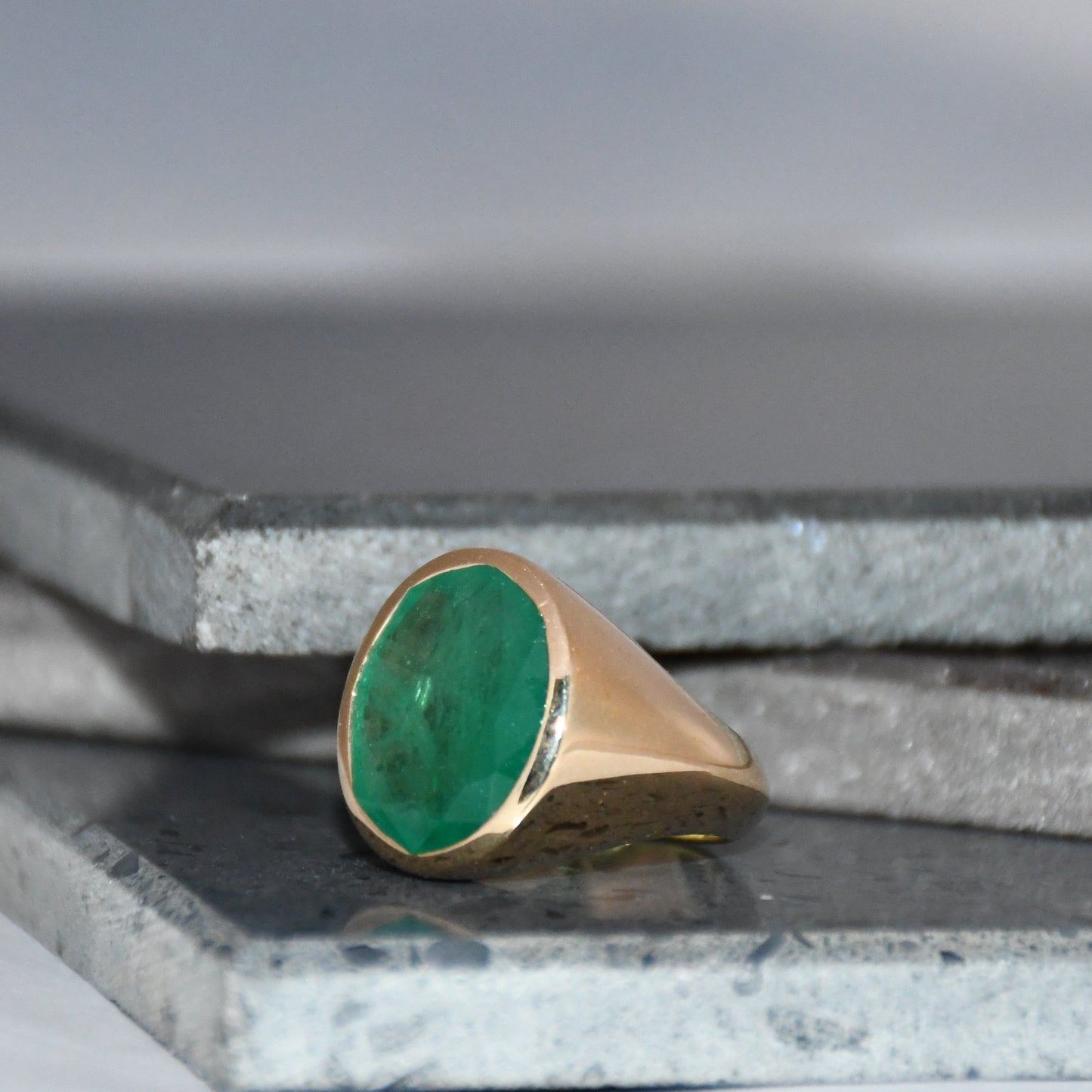 Gold ring with a green emerald gemstone on a gray surface