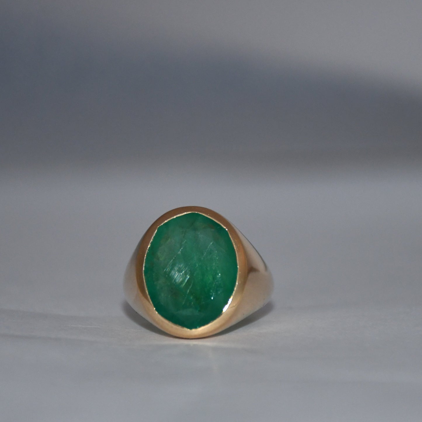 Gold ring with a green emerald gemstone on a gray background