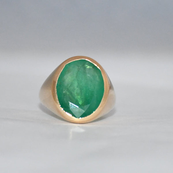 Gold ring with a green emerald stone on a gray background