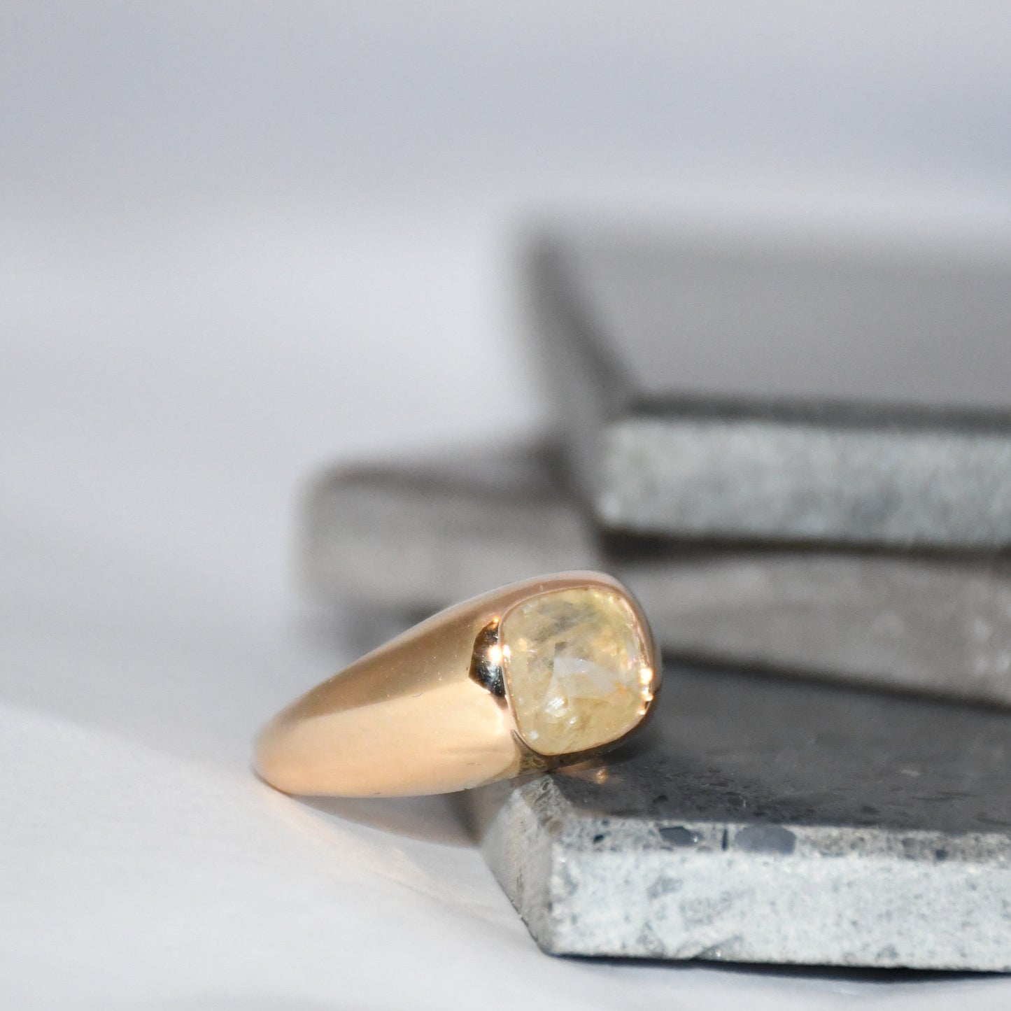 Gold ring with a natural sapphire gemstone on a textured surface with a neutral background