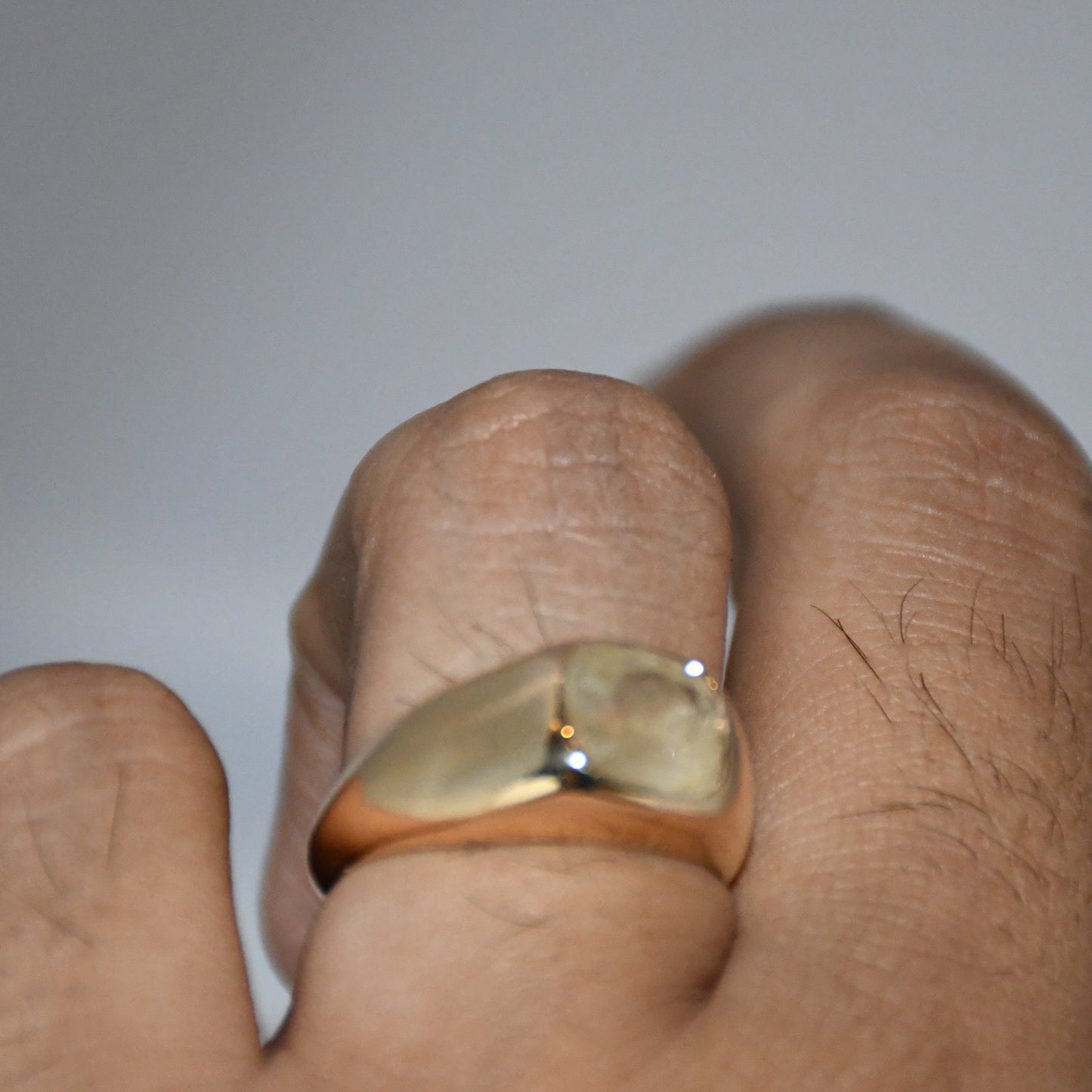 Gold ring with a natural yellow sapphire on a finger against a plain background