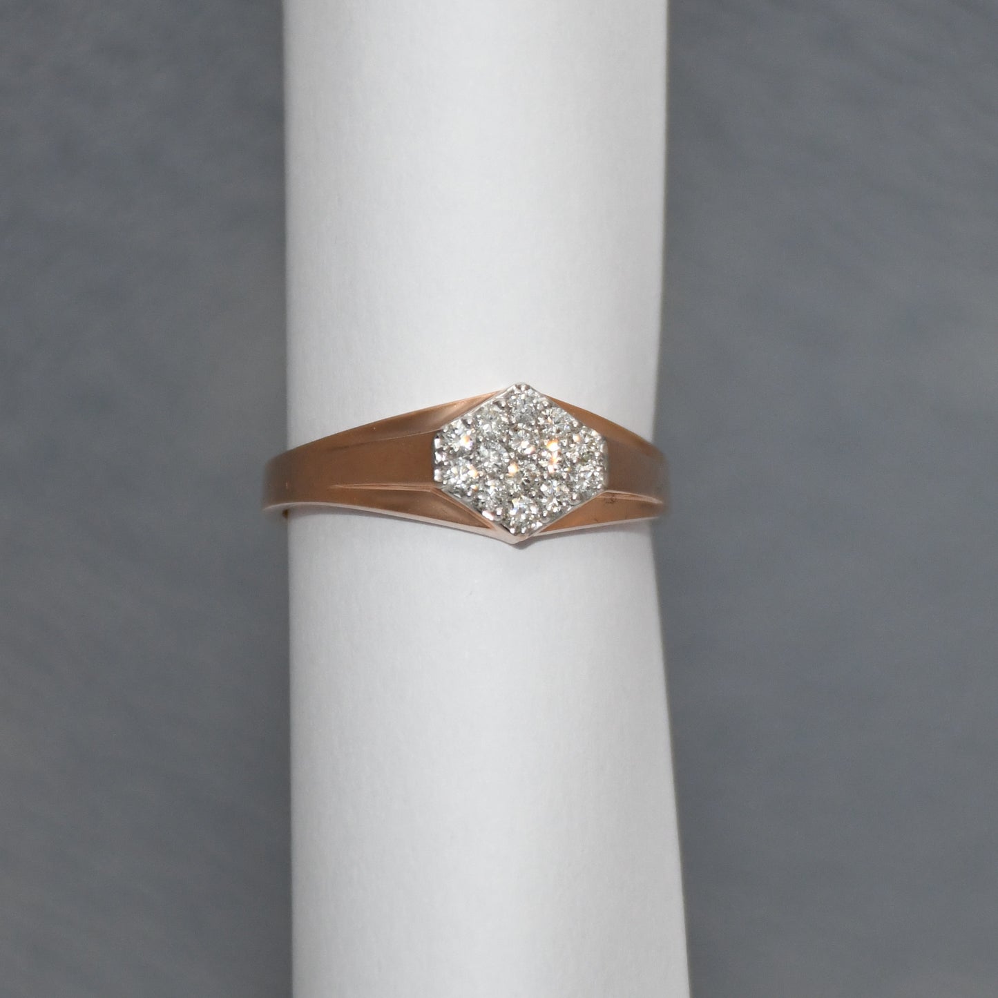 gold ring with diamond on a white cylindrical stand against a gray background