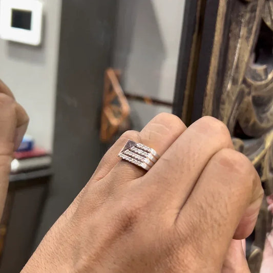 A man's hand displaying a diamond ring with a gold band. The ring has a polished finish with smaller diamonds.