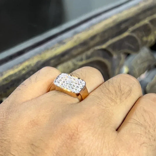 A man's hand holding a pave set diamond ring with a solid gold band, featuring a prominent smaller diamonds along the band.