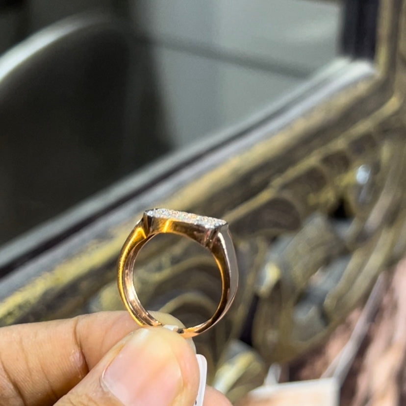 A man's hand holding a pave set diamond ring with a solid gold band, featuring a prominent smaller diamonds along the band.