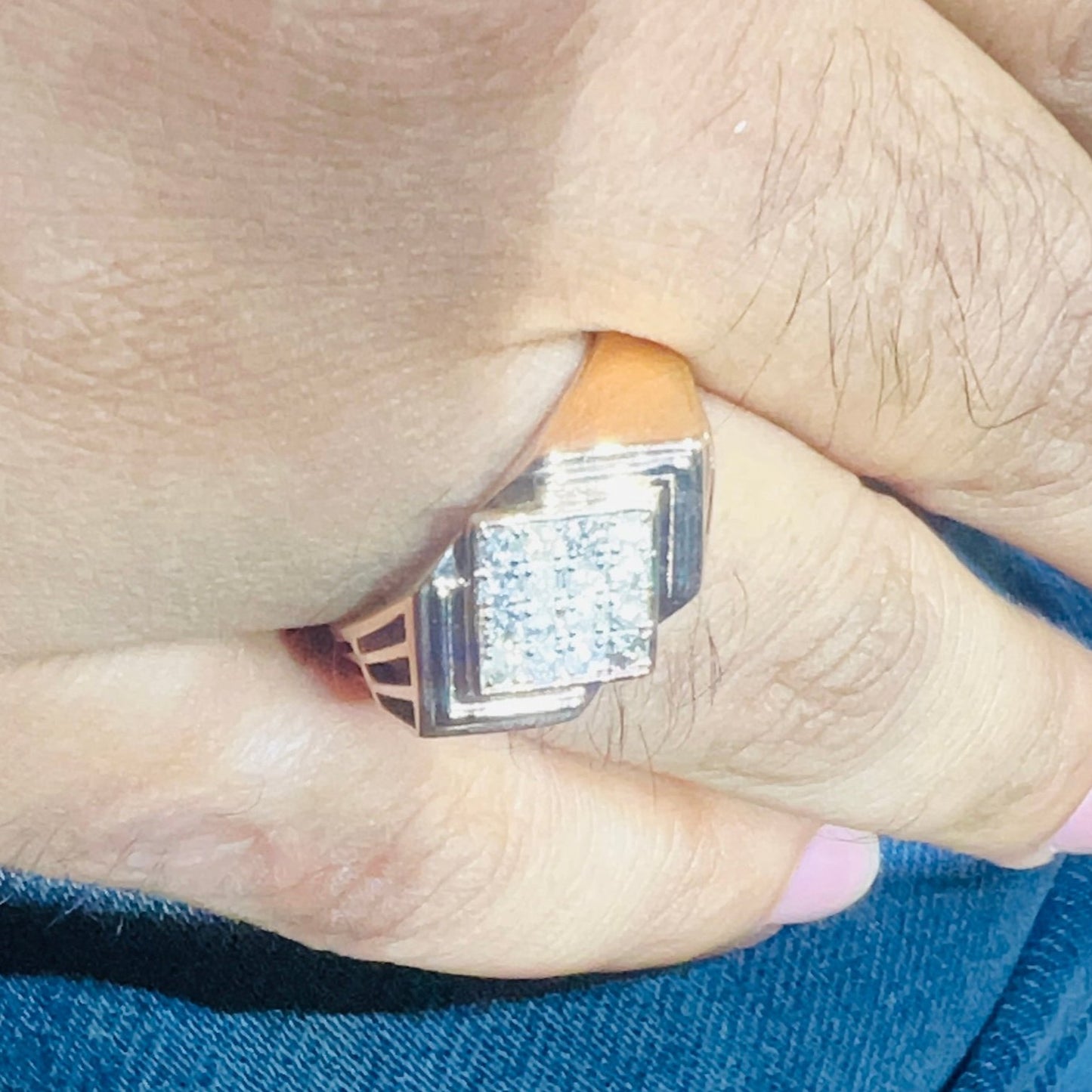 A man's hand holding a diamond ring with a rose gold band, featuring a solitaire diamond on top.