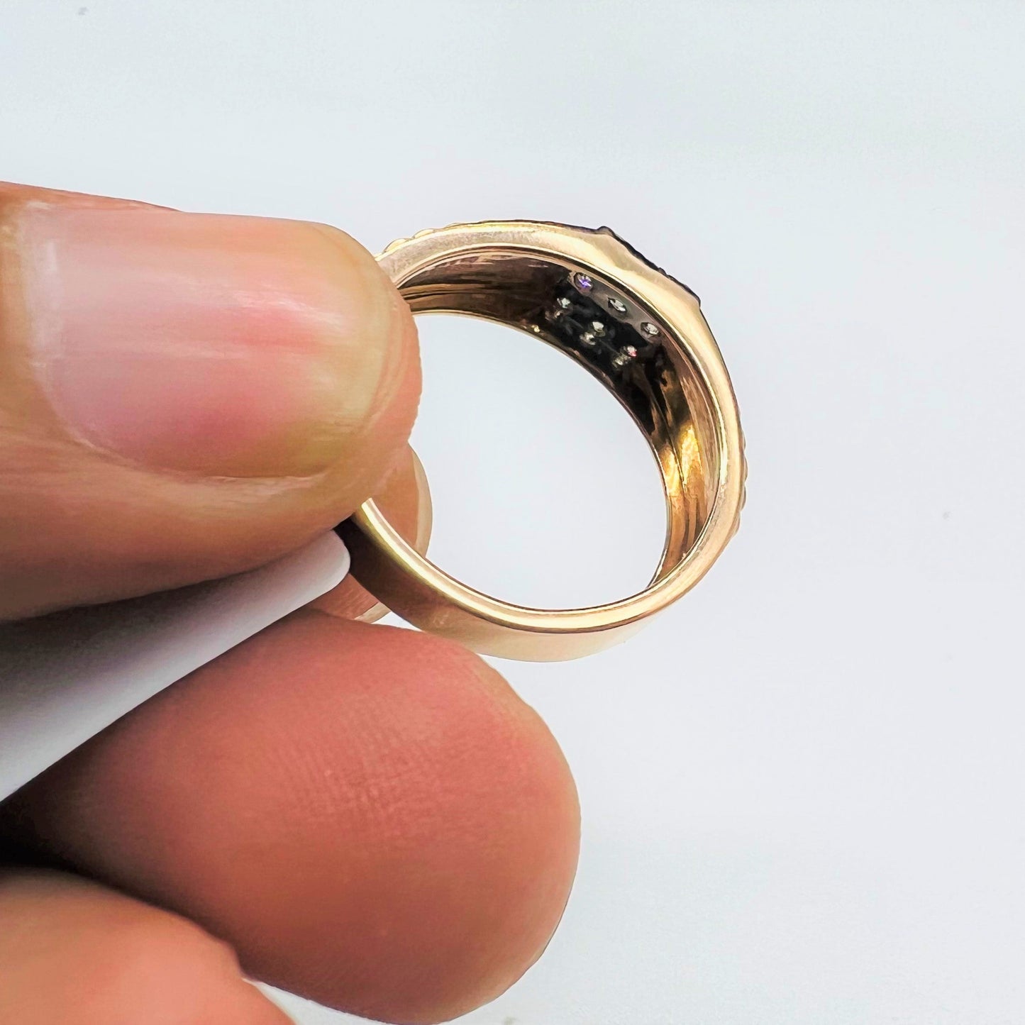 A man's hand holding a gold diamond ring with a solid gold band and a series of round cut diamonds set on top.