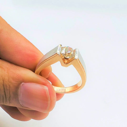 A man's hand holding a solitaire diamond ring with a gold band.