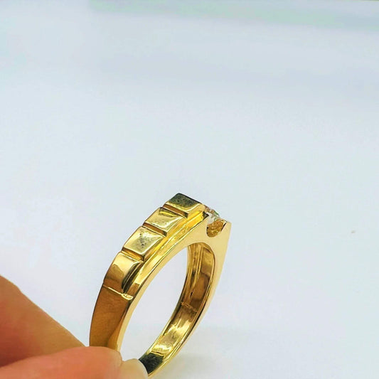A gold band ring with a solitaire round-cut diamond set on top, held between fingers displayed from vertical side.