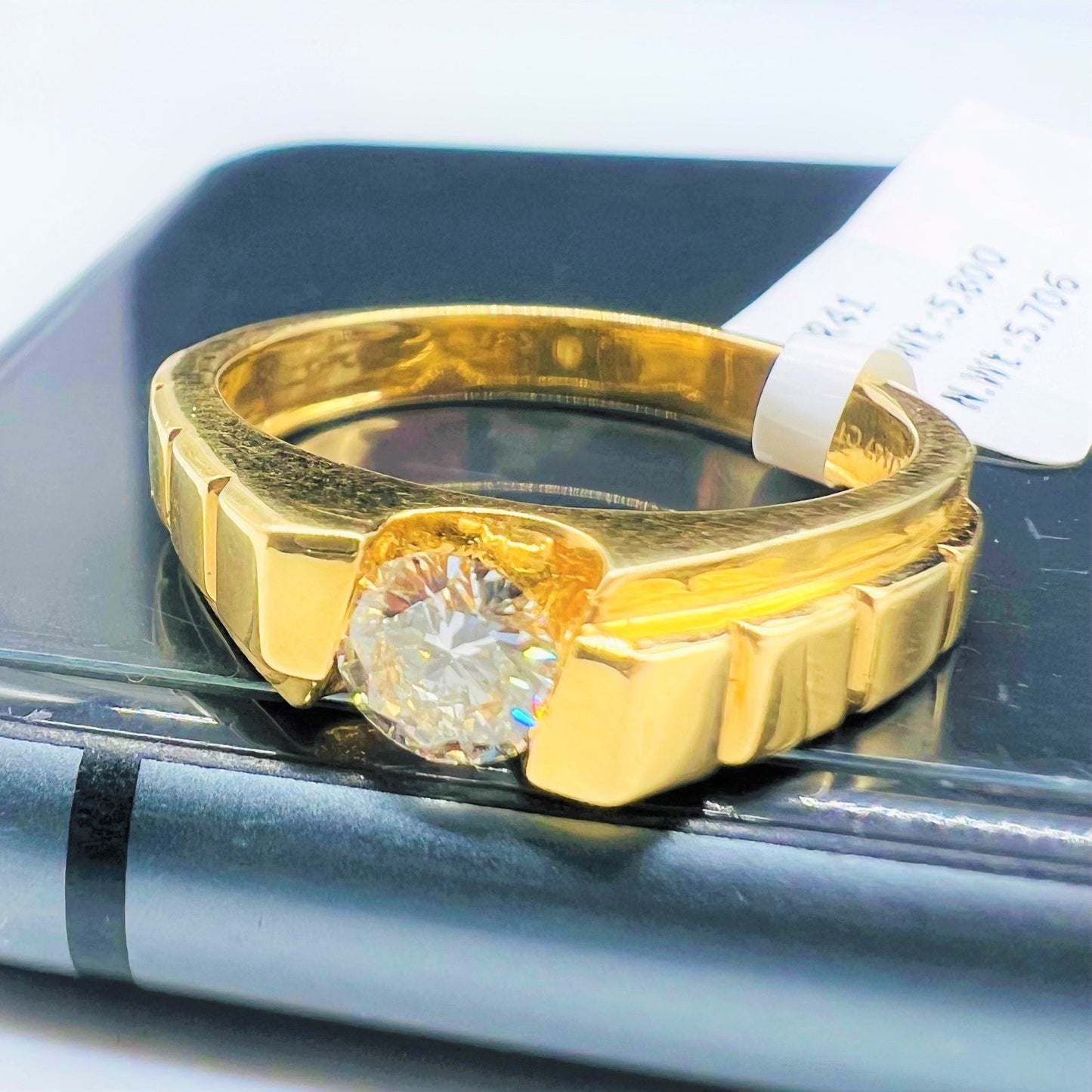 A gold band ring with a solitaire round-cut diamond set on top displayed on a mobile phone.