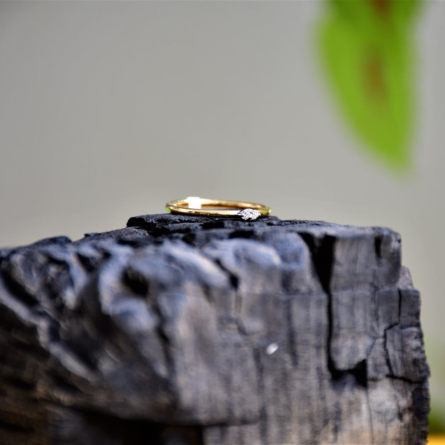A gold band ring with two diamonds set on top, positioned on dark rough stone surface.