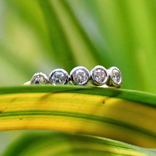 A yellow gold band ring with a series of set diamonds, featuring smaller diamonds, all set in a solid gold band displayed on a light green and yellow leaf.