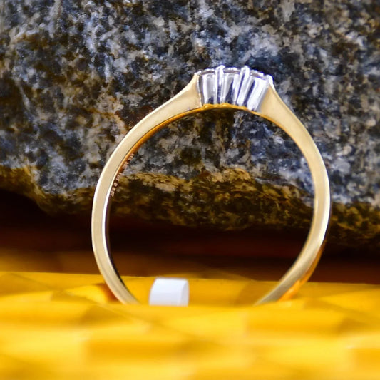A 14kt gold diamond band ring with three brilliant cut natural diamonds on a yellow textured surface.