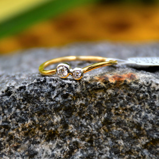 A 14kt gold band ring with two set diamonds on it, placed on a rough textured stone surface.