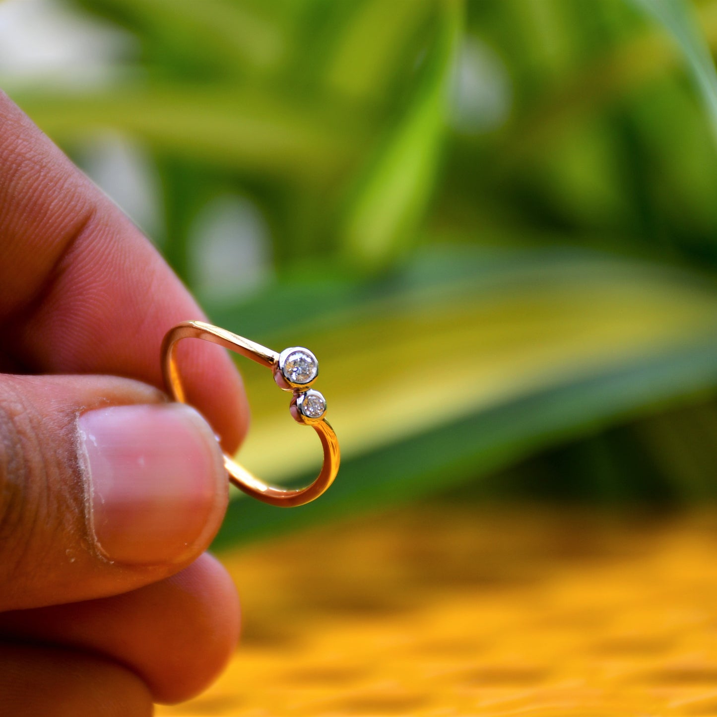 A 14kt gold band ring with two set diamonds on it, held on a hand with green leafy background.