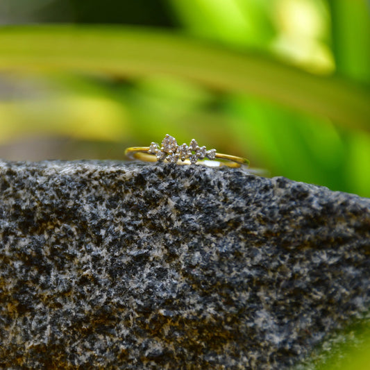 A gold diamond band ring set on a stone surface with a blurred green background.