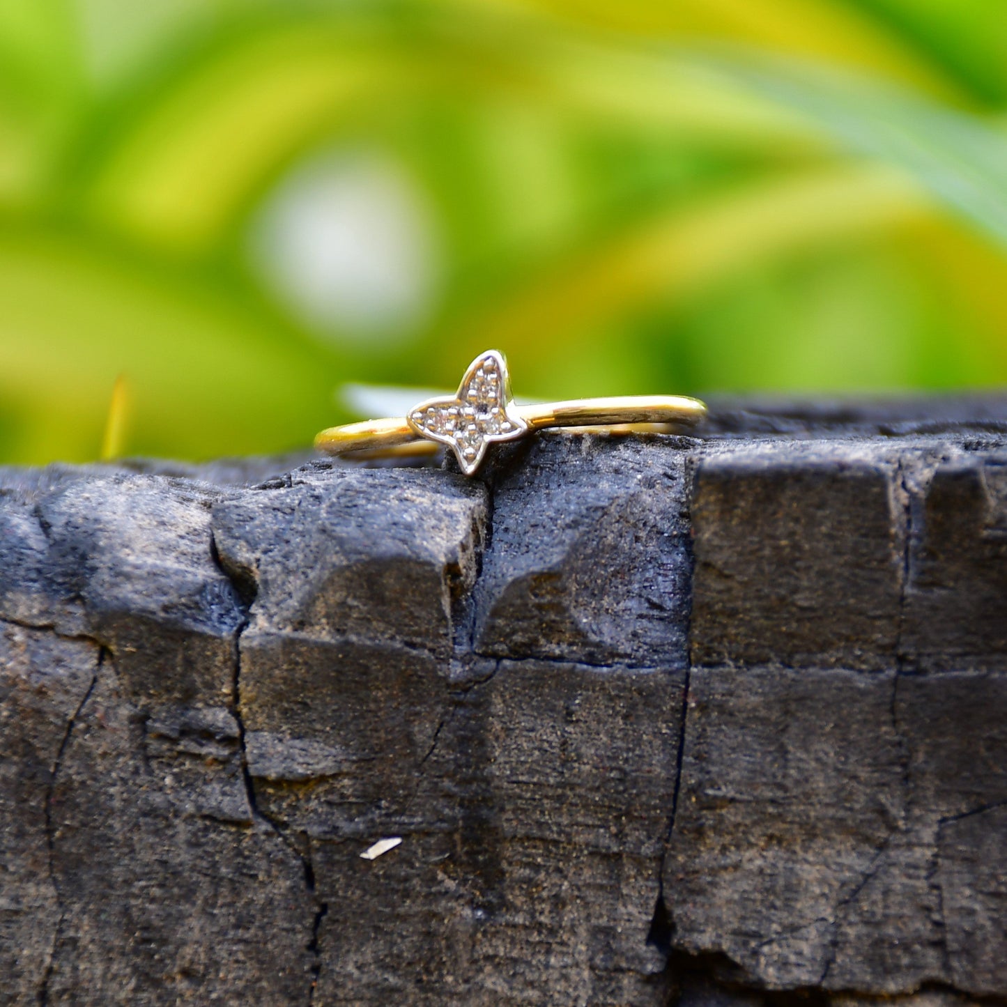 A gold diamond band ring with a butterfly-shape on a rocky surface.