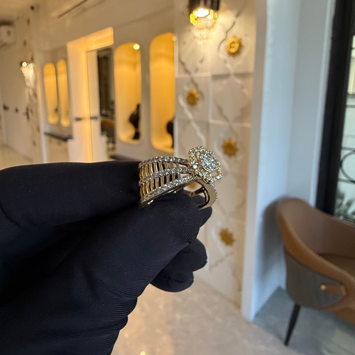 Elegant gold diamond ring featuring a round-cut central diamond surrounded by a halo of smaller diamonds, set on a split shank band adorned with rows of sparkling pavΓ© diamonds, displayed on a black gloved hand against a neutral background.