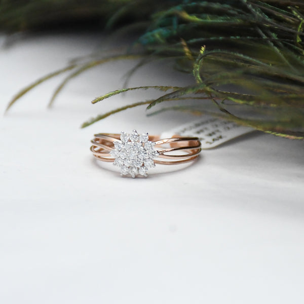 Rose gold ring with diamond accents on a white surface with greenery.