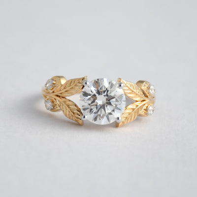 Gold ring with diamond and leaf designs on a light gray background