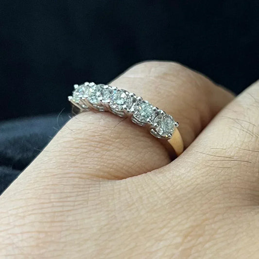 A close-up image of a white gold half eternity ring featuring a row of round brilliant-cut diamonds set in prongs, worn in a finger against a dark background, highlighting the sparkle and detailed craftsmanship of the ring.