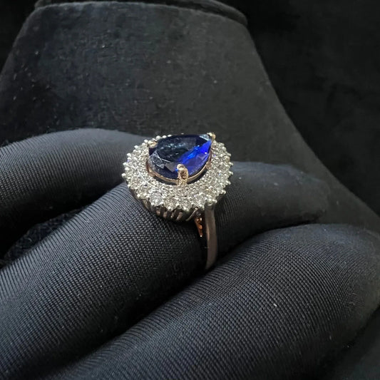 A gold band ring with a sparkling blue color stone and clear diamond set in a brilliant cut, displayed on a black mannequin hand.