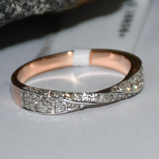 Elegant two-tone diamond ring featuring intertwined bands of rose gold and white gold, adorned with small round-cut diamonds, displayed on a white paper.